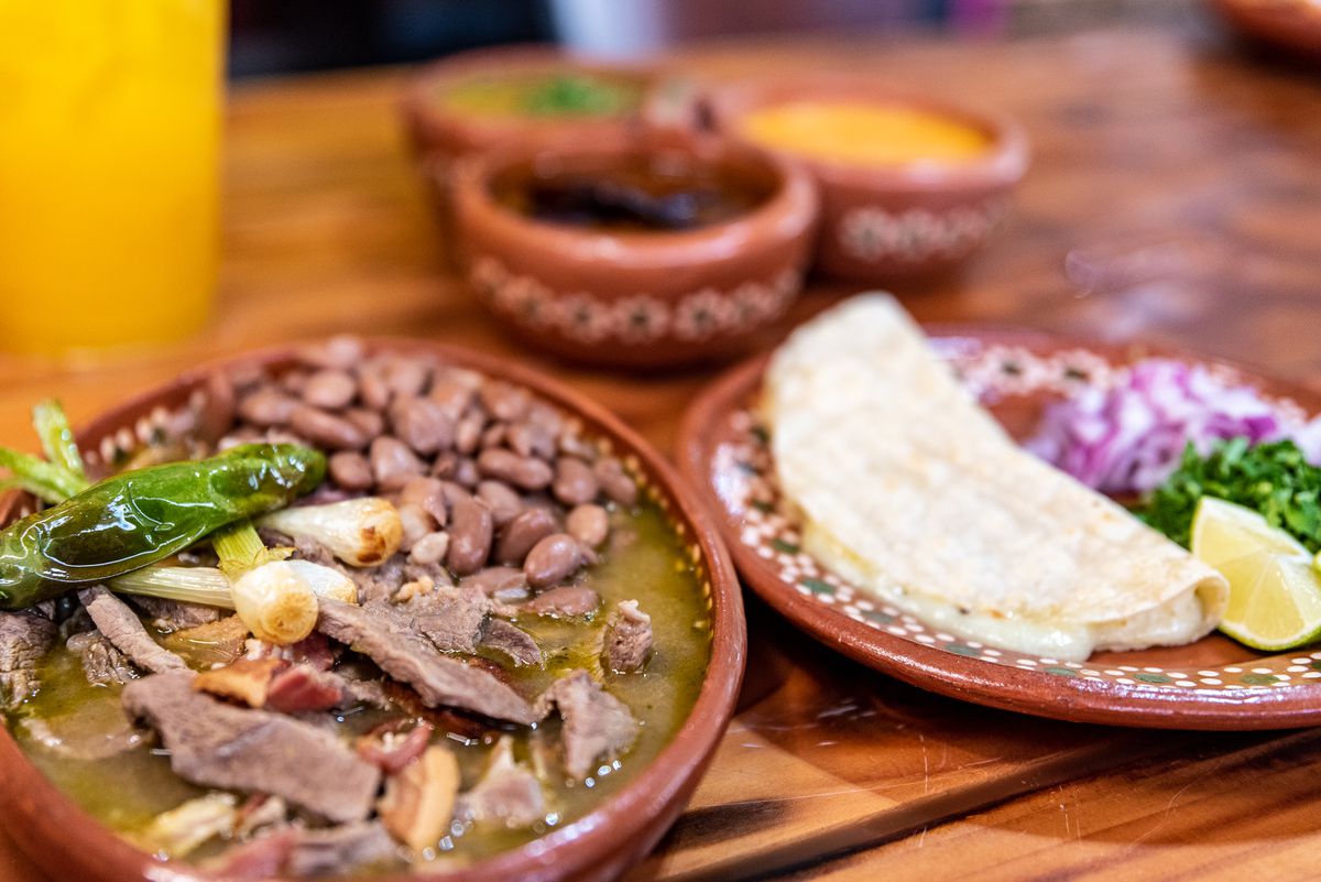 A dish of flank meat and bacon cooked in a tomatillo salsa verde and served with pinto beans, onions, and quesadillas with cilantro and chopped red onions at Carnitas El Artista.