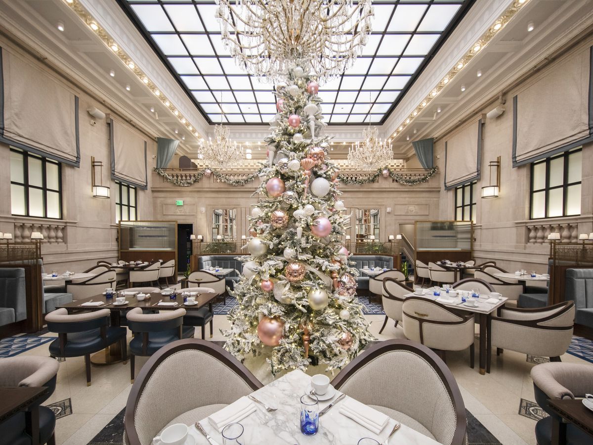 A high-ceilinged, light-filled restaurant dining room with pink and white-themed Christmas trees placed around tables and chairs.