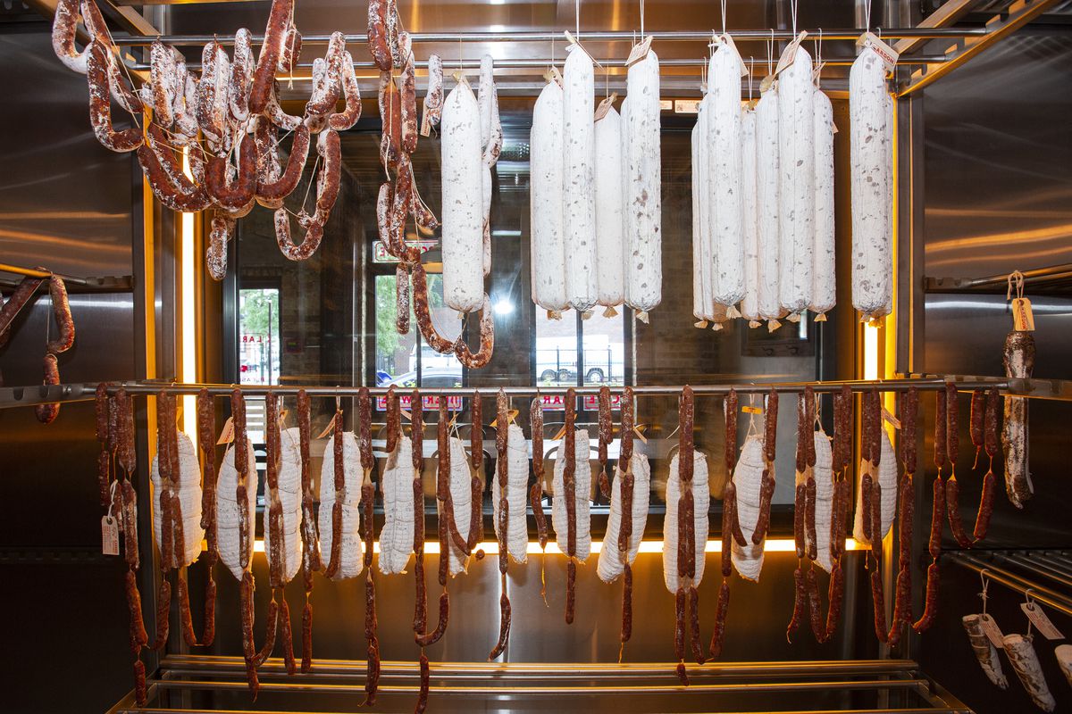 Cured meats hang inside a metal room.