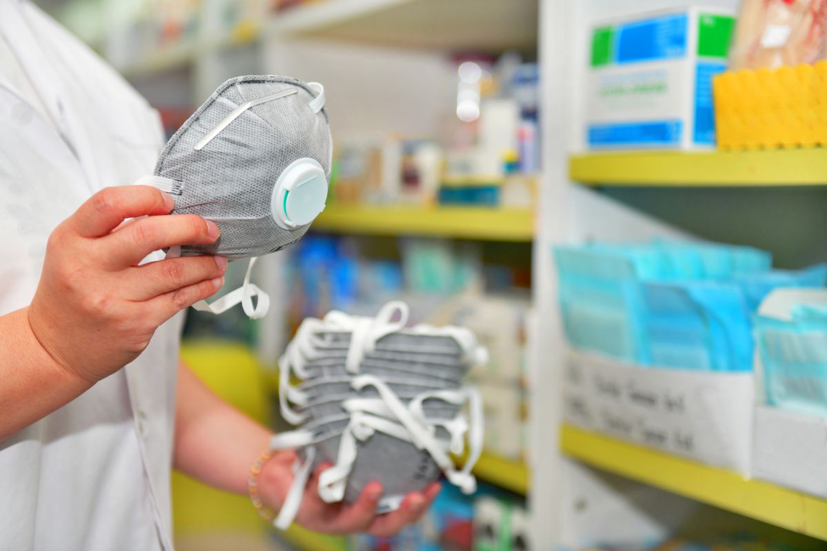 A pharmacist holds a gray N95 respirator in her hand.
