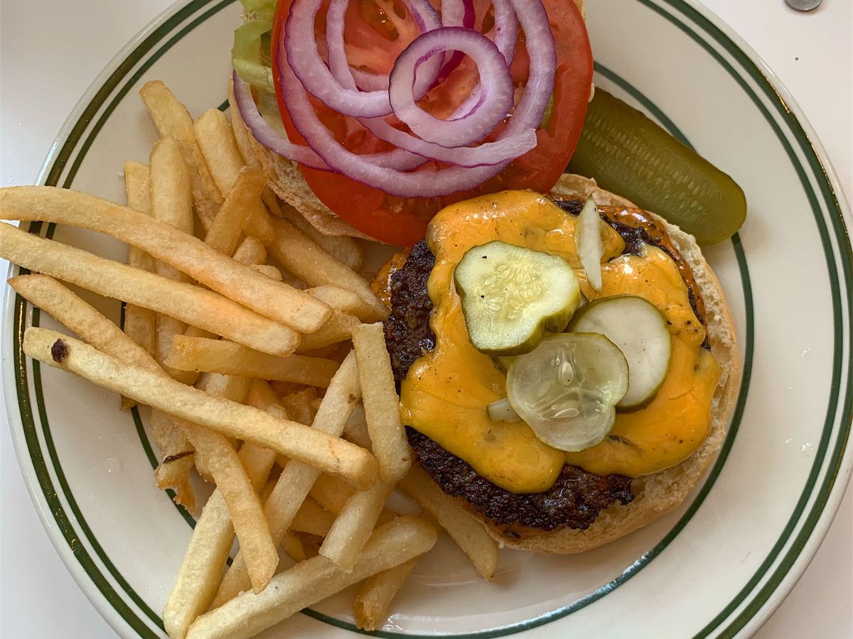 A cheeseburger with three pickles on top, plus fries, on a white plate with a striped lining.