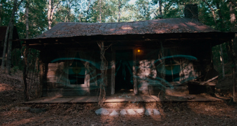A spooky pair of eyes superimposed over a run-down looking cabin in a shot from Evil Dead 2
