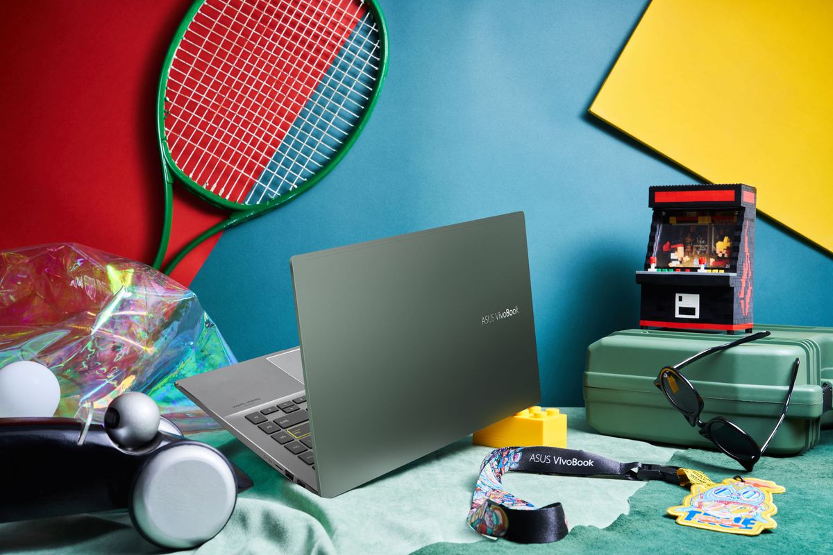 The VivoBook S14, open, faces away from the camera next to a pile of accessories including a tennis racket, a toolbox, and a pair of sunglasses.