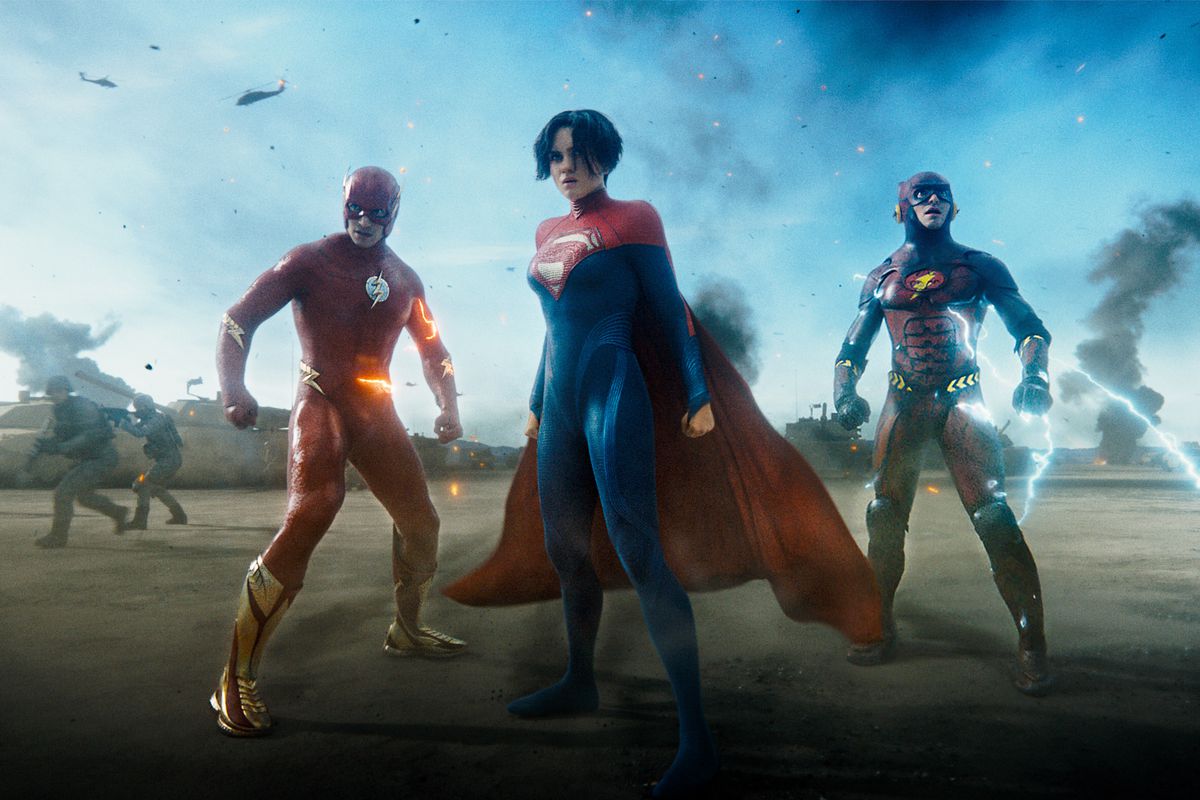 Supergirl stands in front of Barry Allen and his younger self, each in their own Flash costume, on a battlefield surrounded by Kryptonian soldiers in the film The Flash