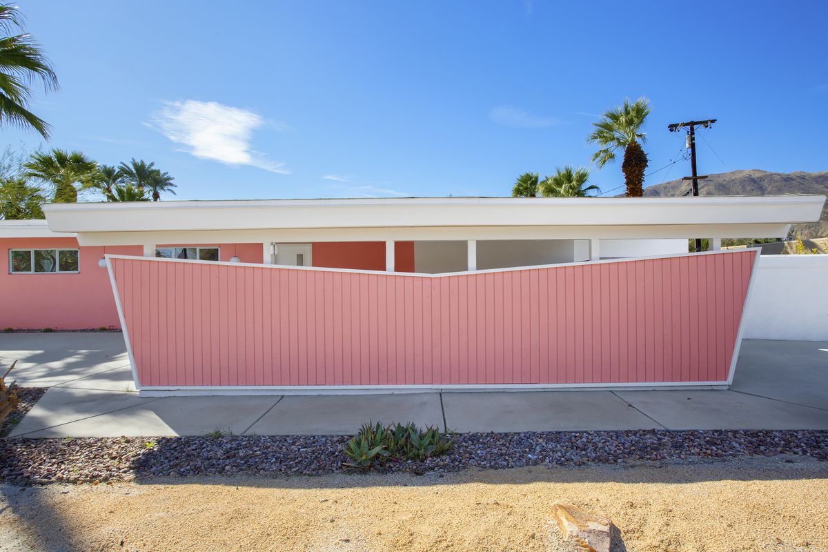 An exterior view of a midcentury modern house with carport. The house is bright pink with white trim. 