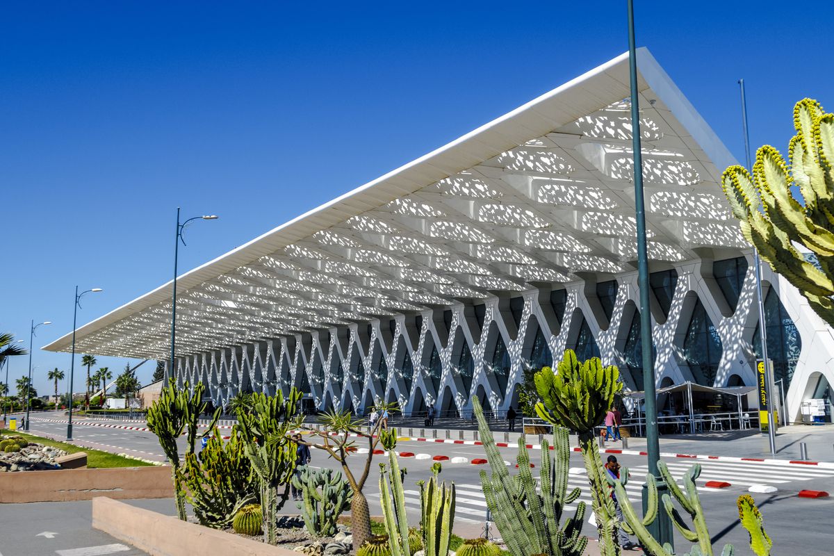 The exterior of the Marrakech Menara airport in Morocco. The facade is white and has an ornamental design. The roof is sloped upwards.