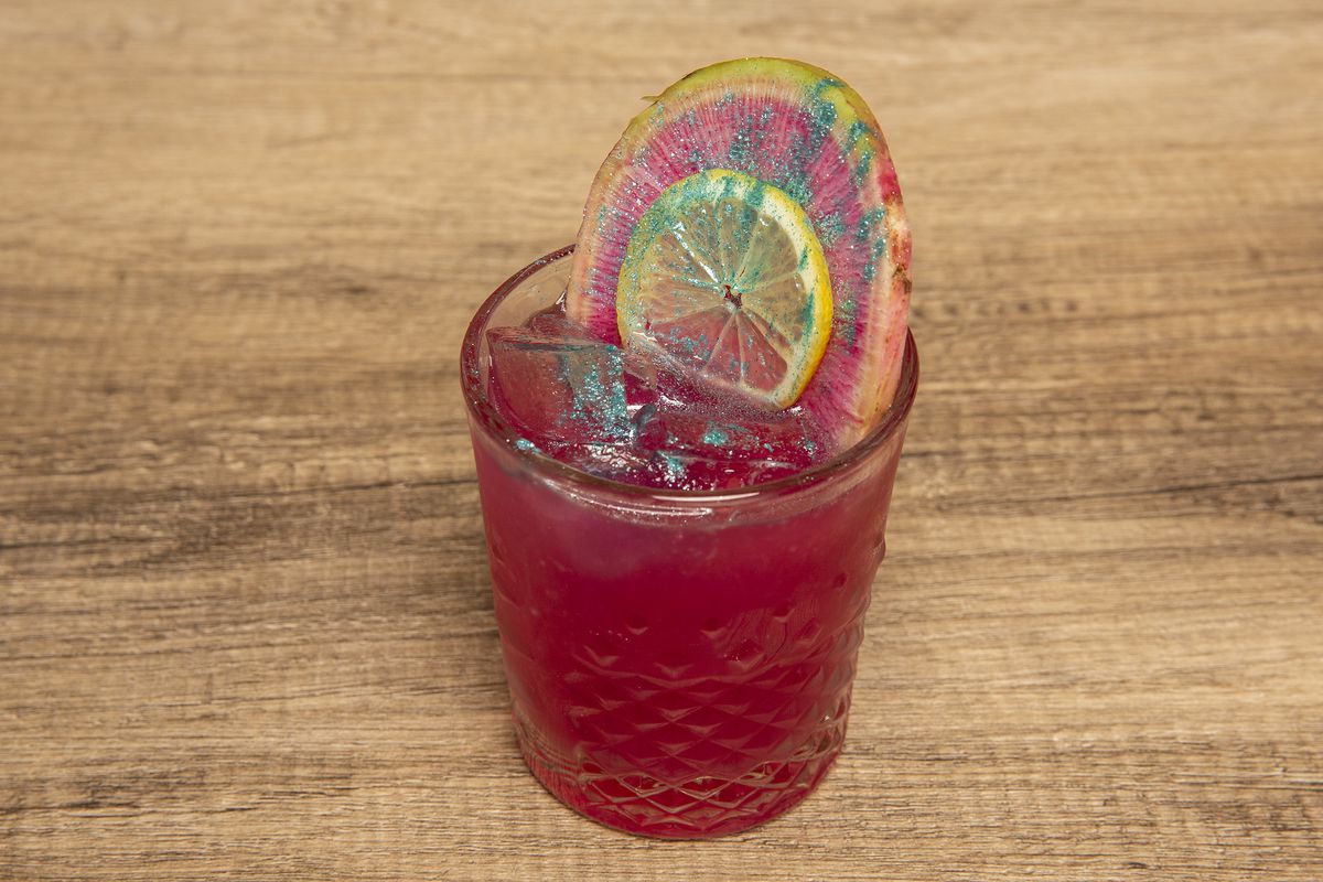 A pink drink garnished with a lemon and blue glitter.