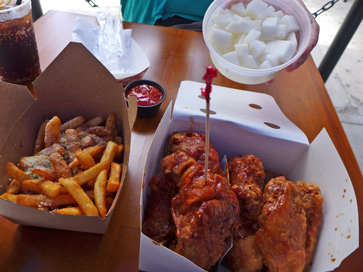 A box of sticky looking fried chicken, with french fry and cubed radish sides.