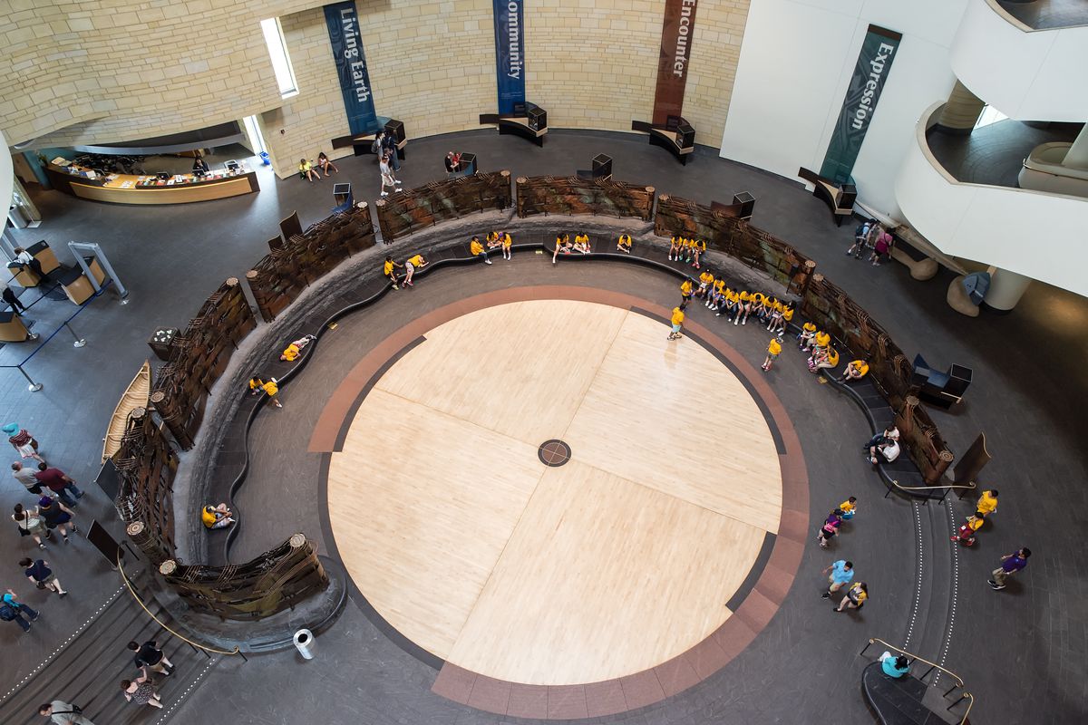 A dance circle in the middle of a museum floor. Curved seating frames the circle and there are children around it.