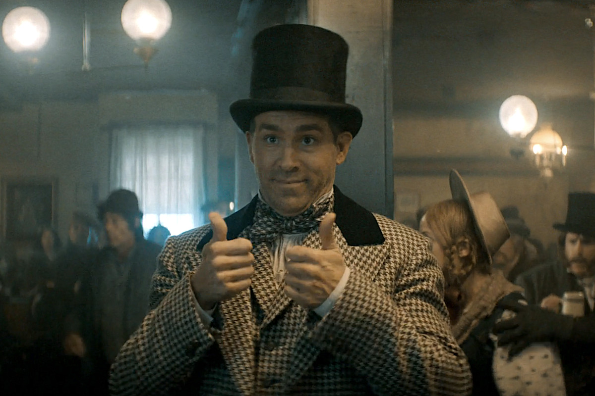 Ryan Reynolds as smug marketer Clint Briggs in Spirited, wearing a Dickens-era top hat and suit, and smirking and offering a double thumbs up during the “Good Afternoon” song