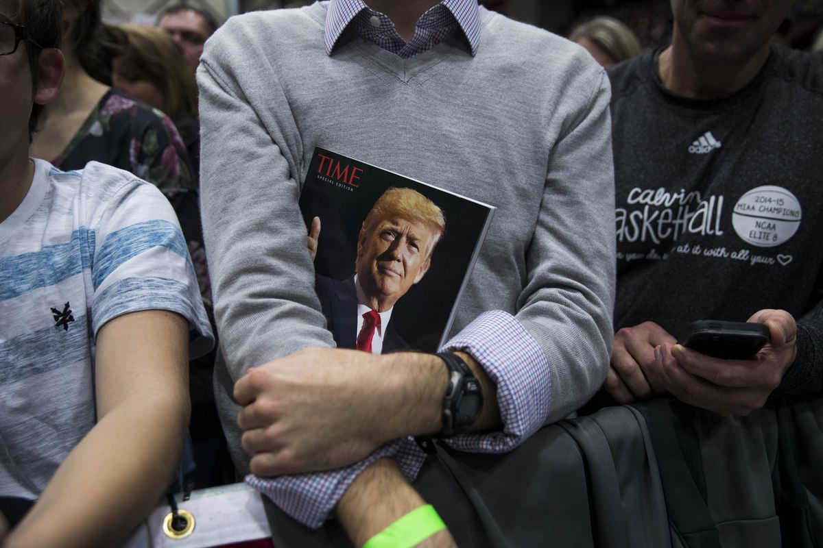A man holding a copy of Time magazine with President Trump’s face on the cover