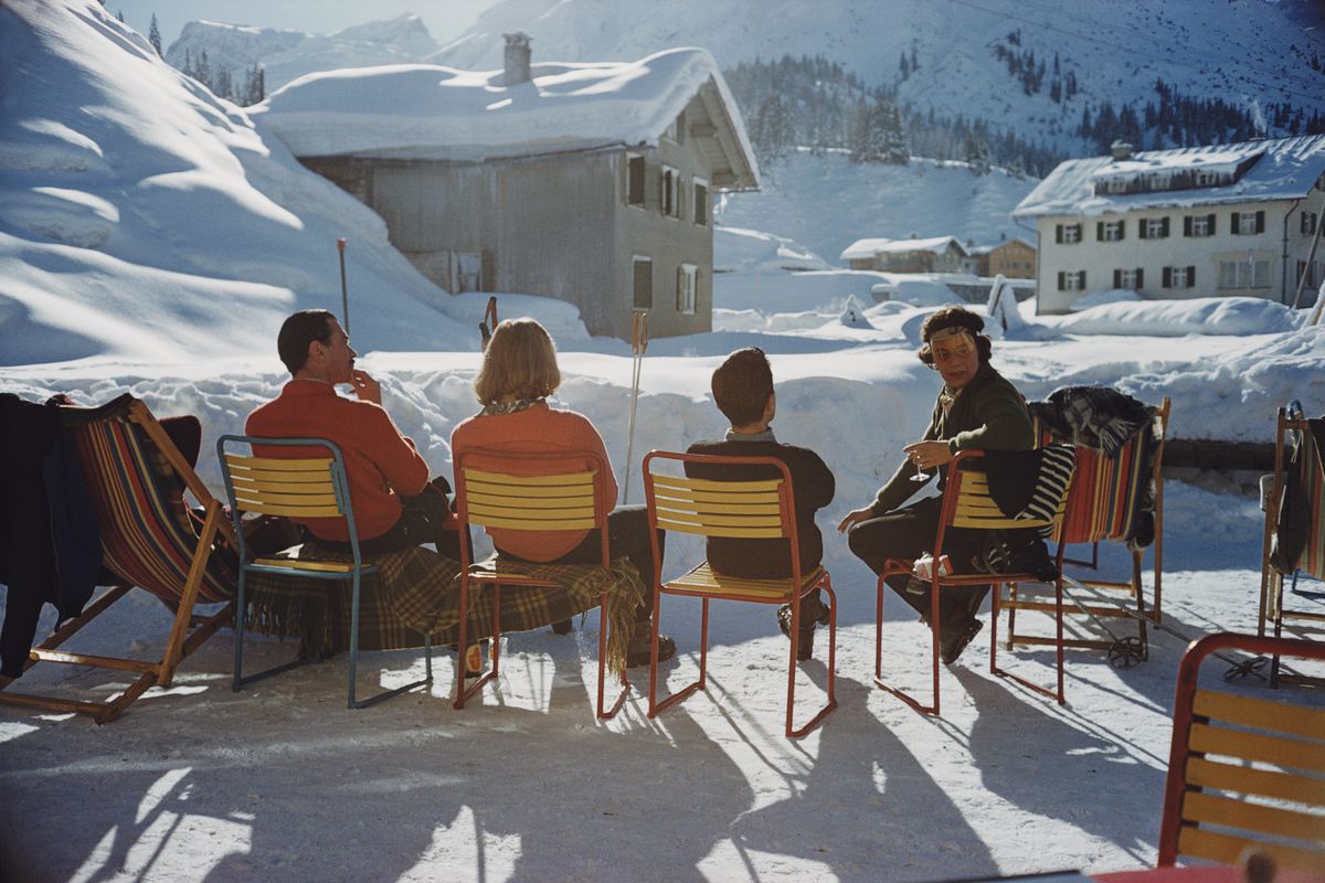 A vintage photograph of four people in patio chairs looking out on a snowy town and mountain.