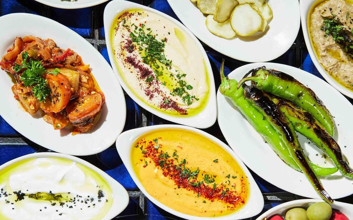 From above, a table full of colorful dishes, including whole grilled peppers, dips, and pickles.