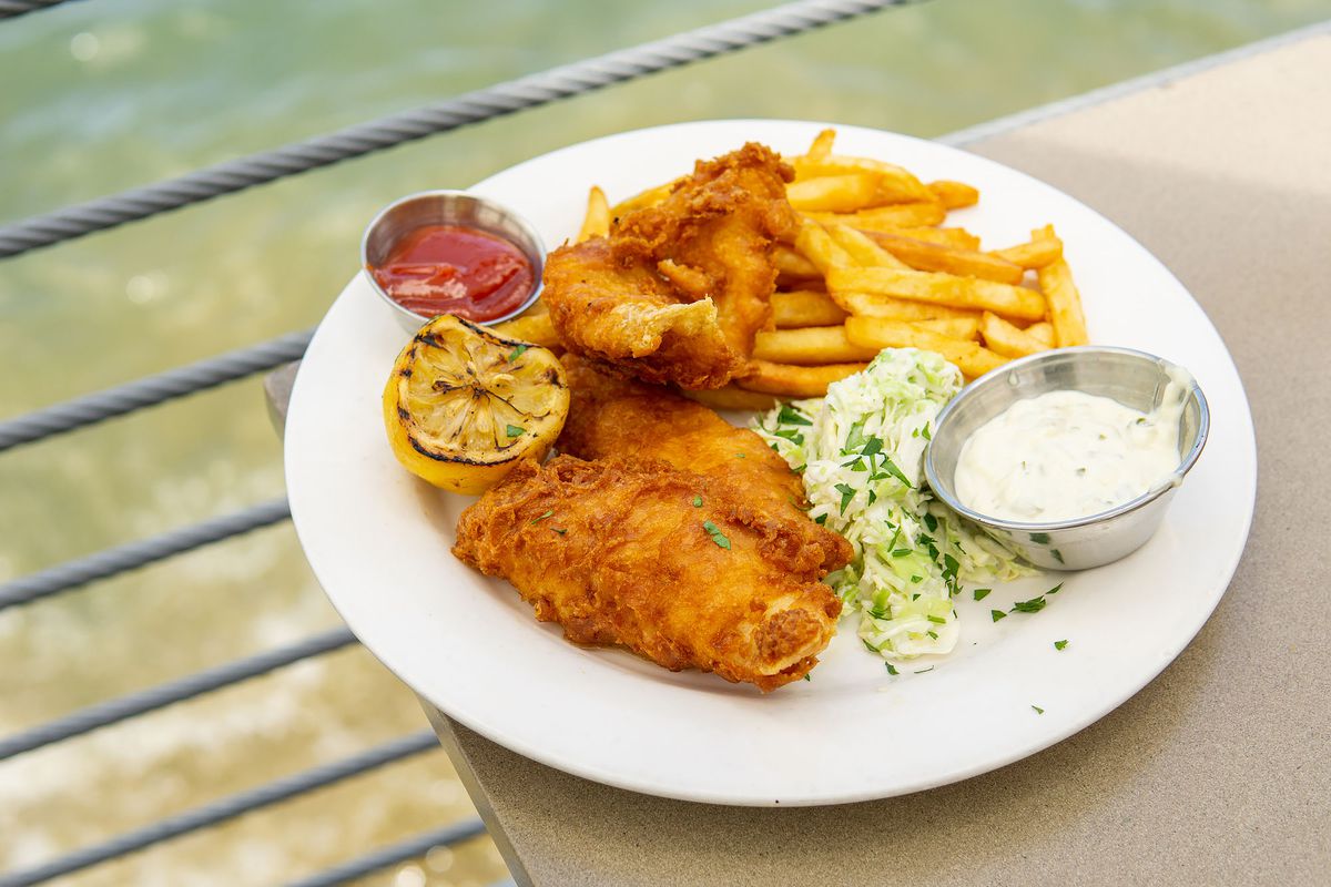 A platter of fried fish and french fries at daytime along the water.