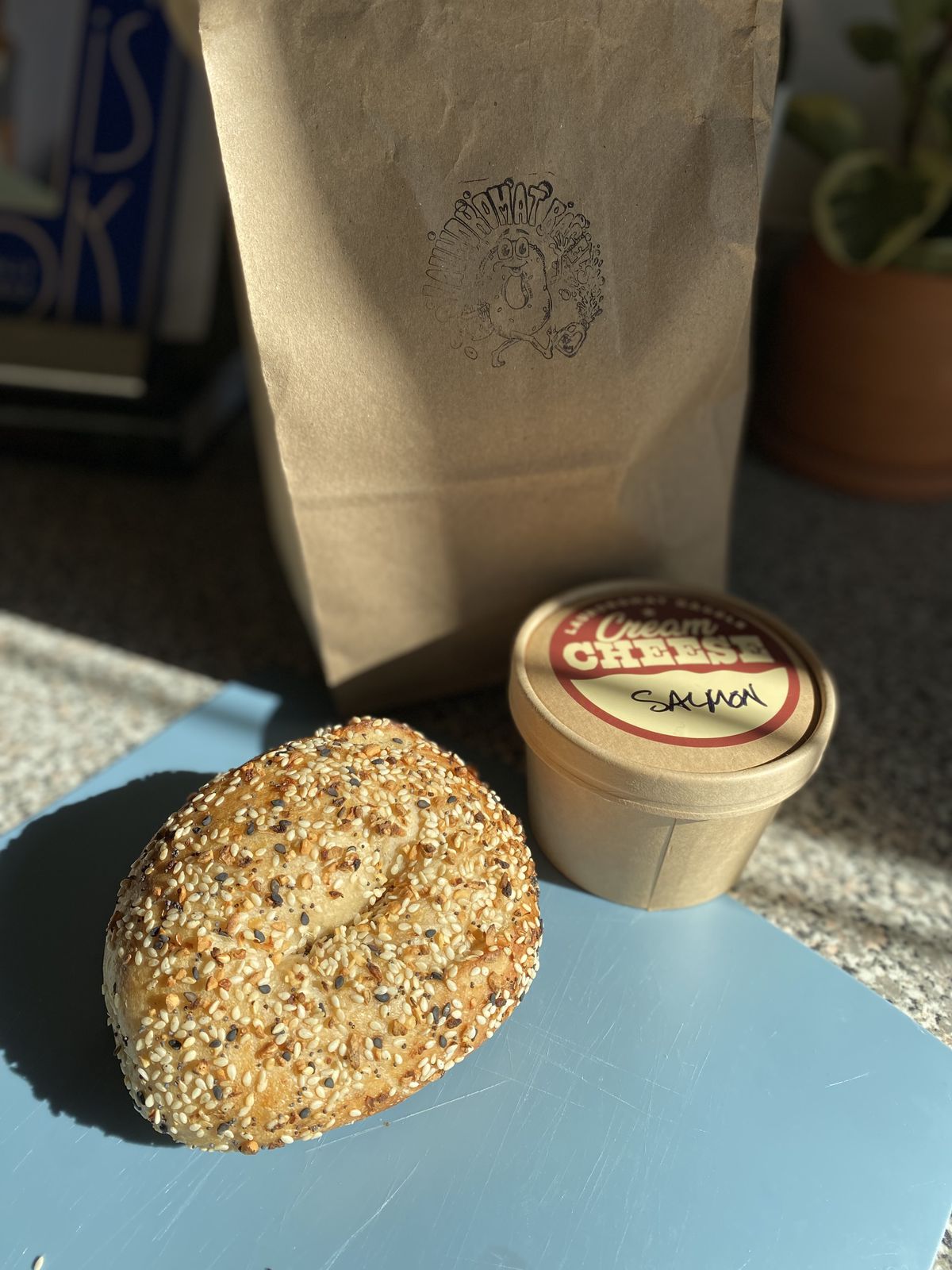 An everything bagel with a container of schmear on a counter. 