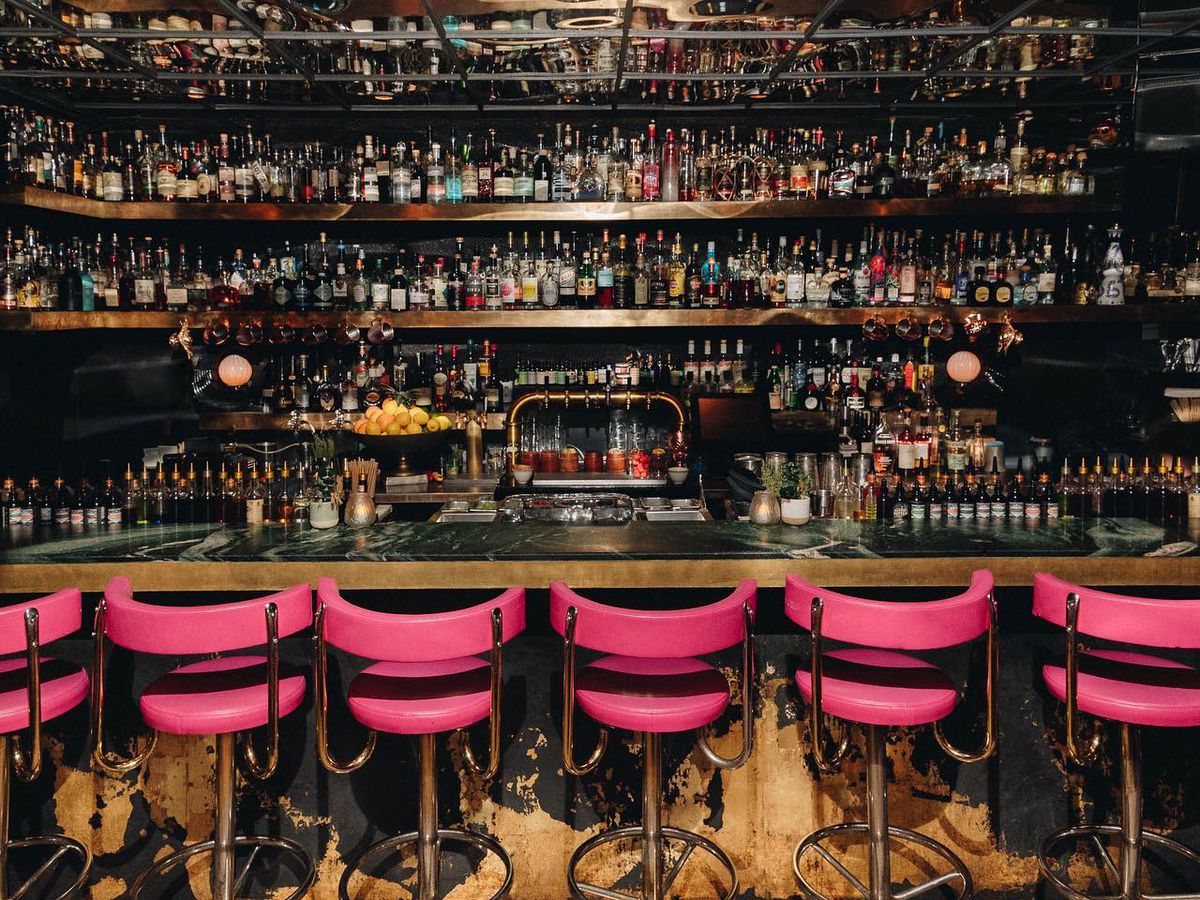 A bar lined with bottles with magenta chairs.