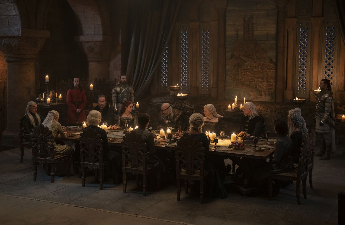 Many Targaryens from House of the Dragon sit around a large table with food on it during a dinner