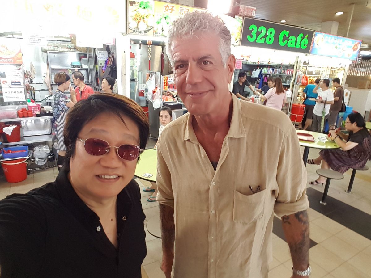 A portrait of Singaporean street food expert KF Seetoh in a black shirt and sunglasses next to Anthony Bourdain, the celebrity chef, writer, and TV host in a khaki color shirt. Both standing in a Singapore hawker center.