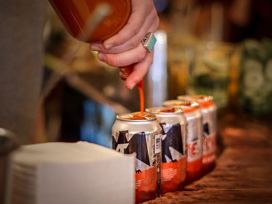 A bartender pours hot sauce atop Tecate beers.