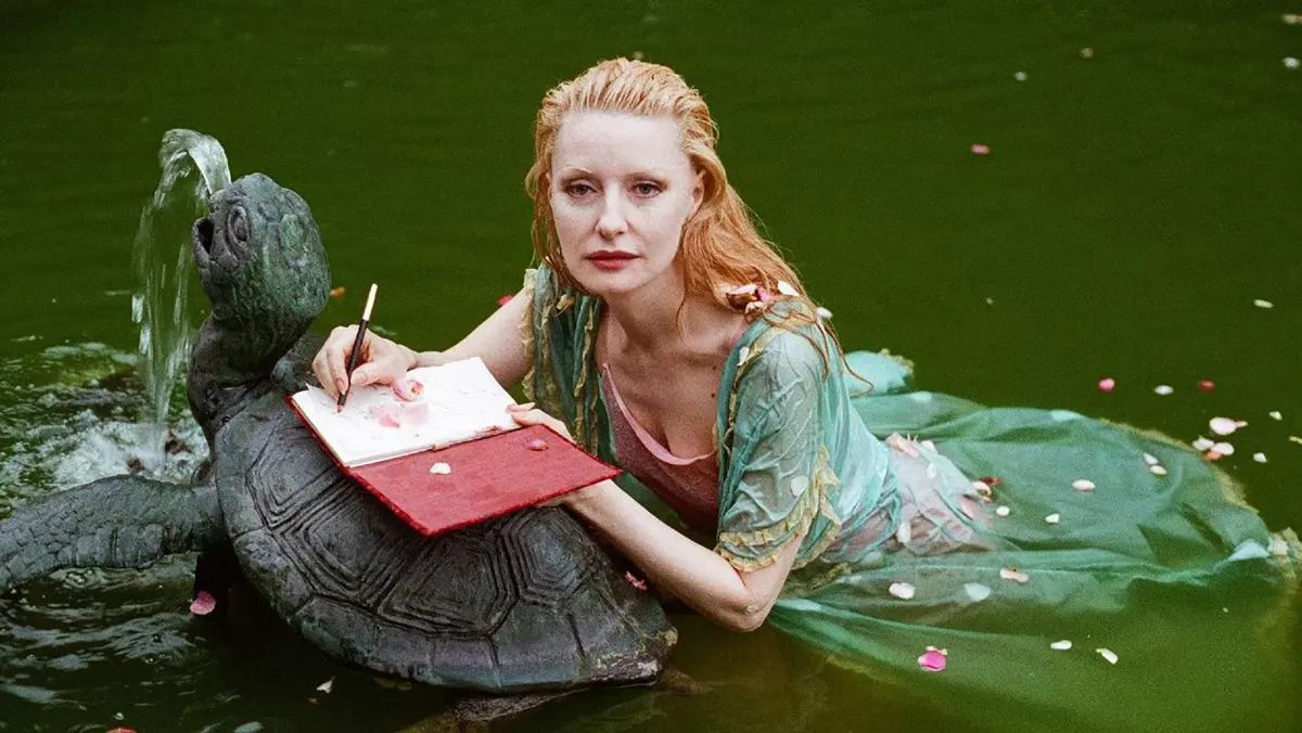 Photo Shere Hite lying in a pool of water writing in a red journal atop a stone turtle fountain in the documentary “The Disappearance of Shere Hite.”&nbsp;