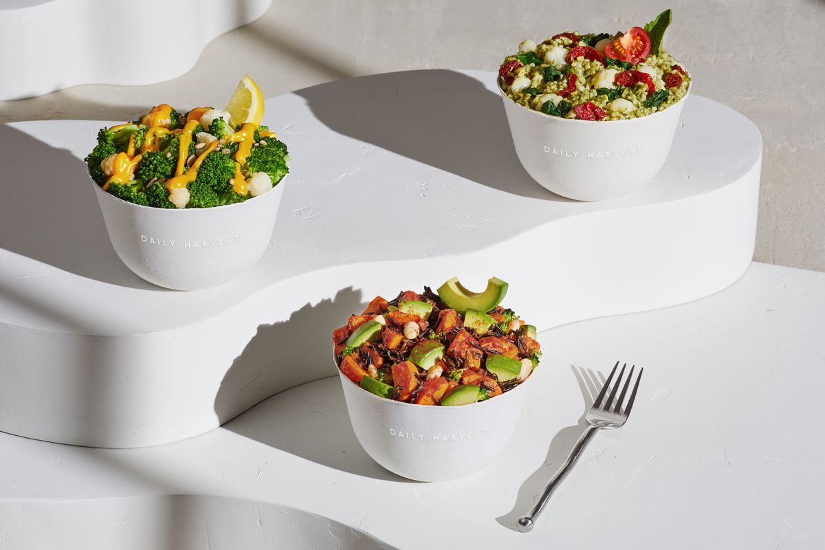Three white bowls filled with healthy-looking food arranged on white risers