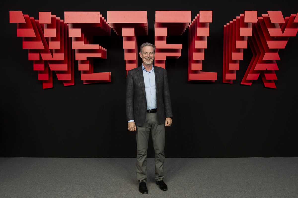 Reed Hastings standing in front of a large sign that says “Netflix.”