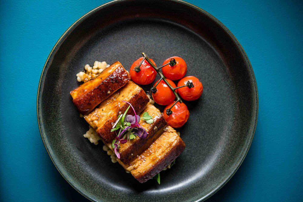 Overhead black plate of pork belly and roasted tomatoes.