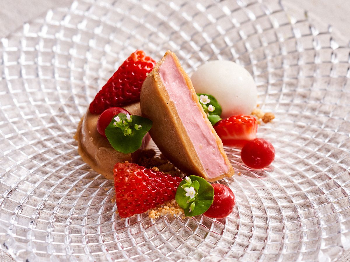 A strawberry ice cream sandwich is plated next to slices of strawberry and flowers from Anomaly, a San Francisco restaurant from chef Mike Lanham.