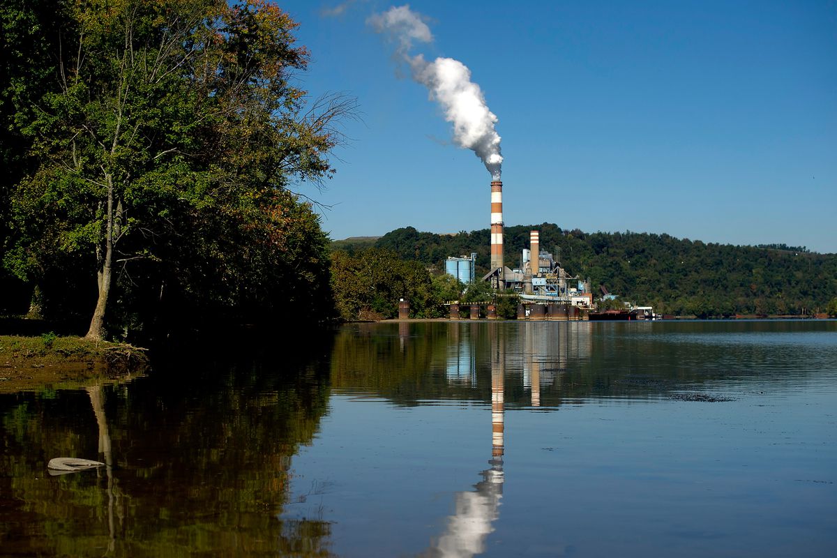 A power plant at the edge of a lake belches steam from its smokestack.