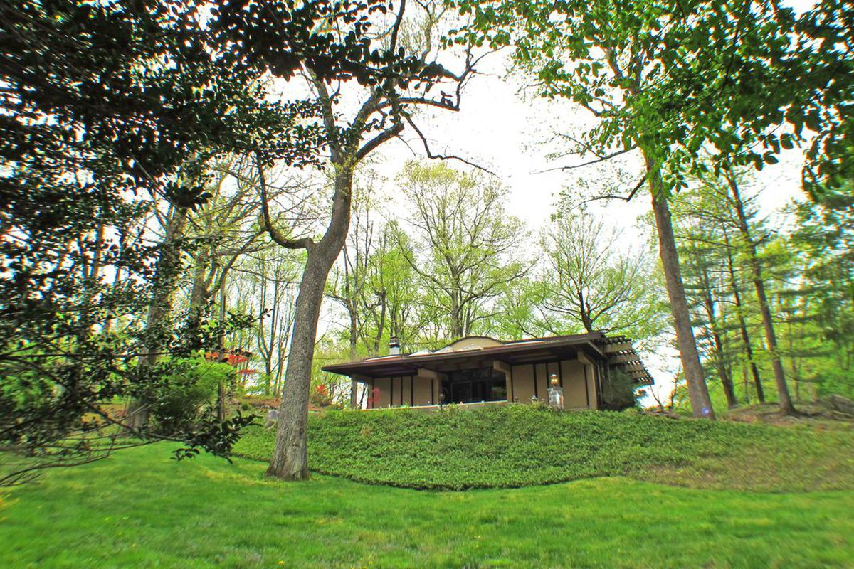 Exterior shot of post-and-beam home with overhanging roof and a set on a grassy hillside site. 