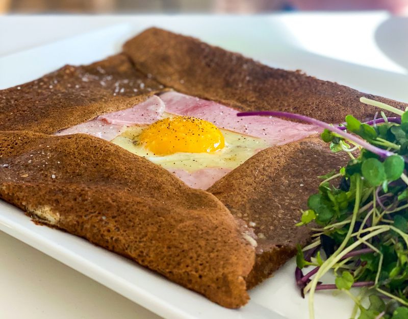 A square-shaped crepe filled with ham and cheese and a side salad on a white plate.