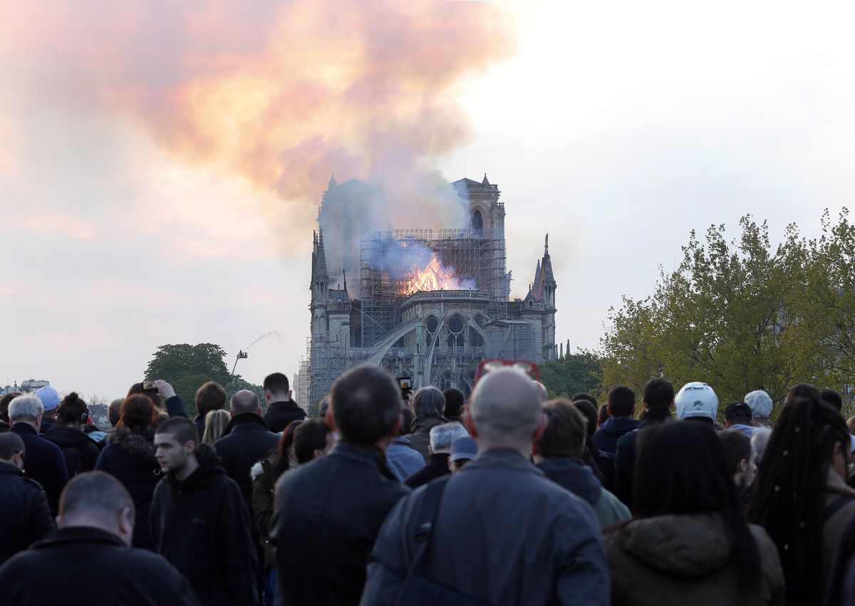 People watch as flames and smoke rise from Notre Dame cathedral as it burns in Paris, Monday, April 15, 2019. Massive plumes of yellow brown smoke is filling the air above Notre Dame Cathedral and ash is falling on tourists and others around the island th
