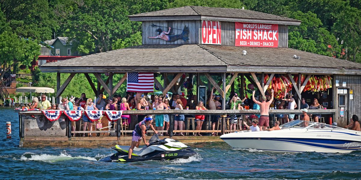 A person on a Jet Ski and people on a motorboat move past a crowded restaurant-bar built on a water-level pier on the lake.