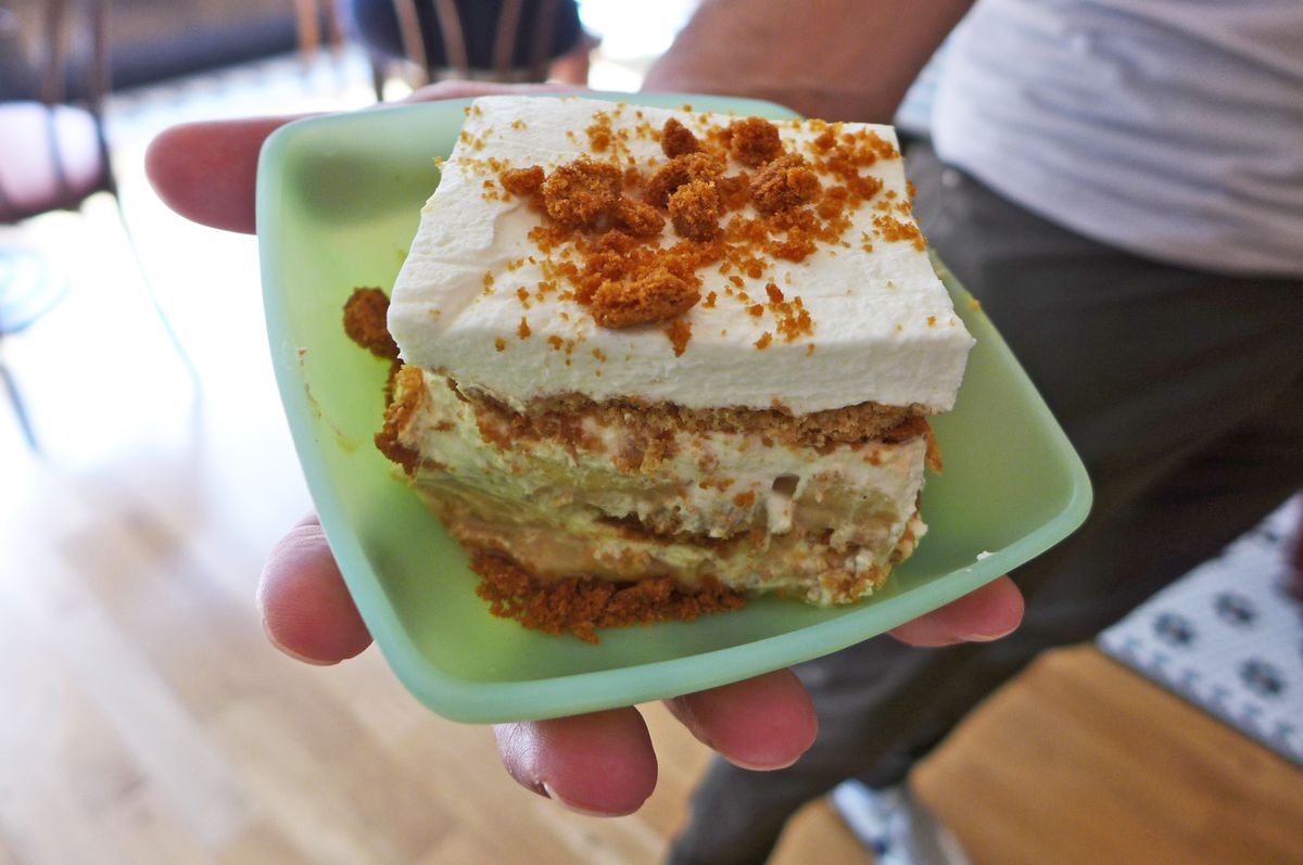 A square of whipped cream, caramel, and graham crumb caked held aloft by a pair of hands.