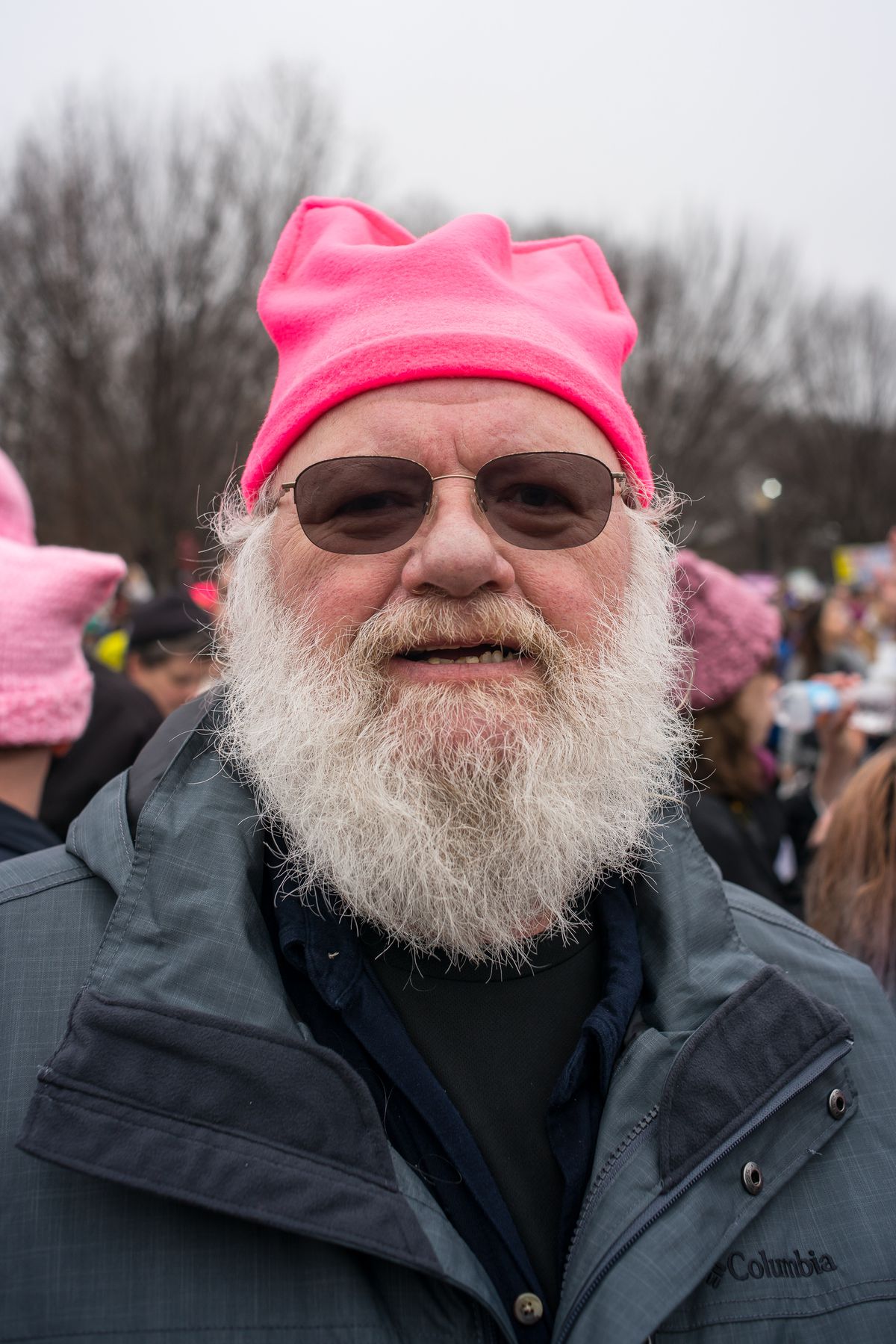 An older man with a white beard wears a hot pink pussy hat.