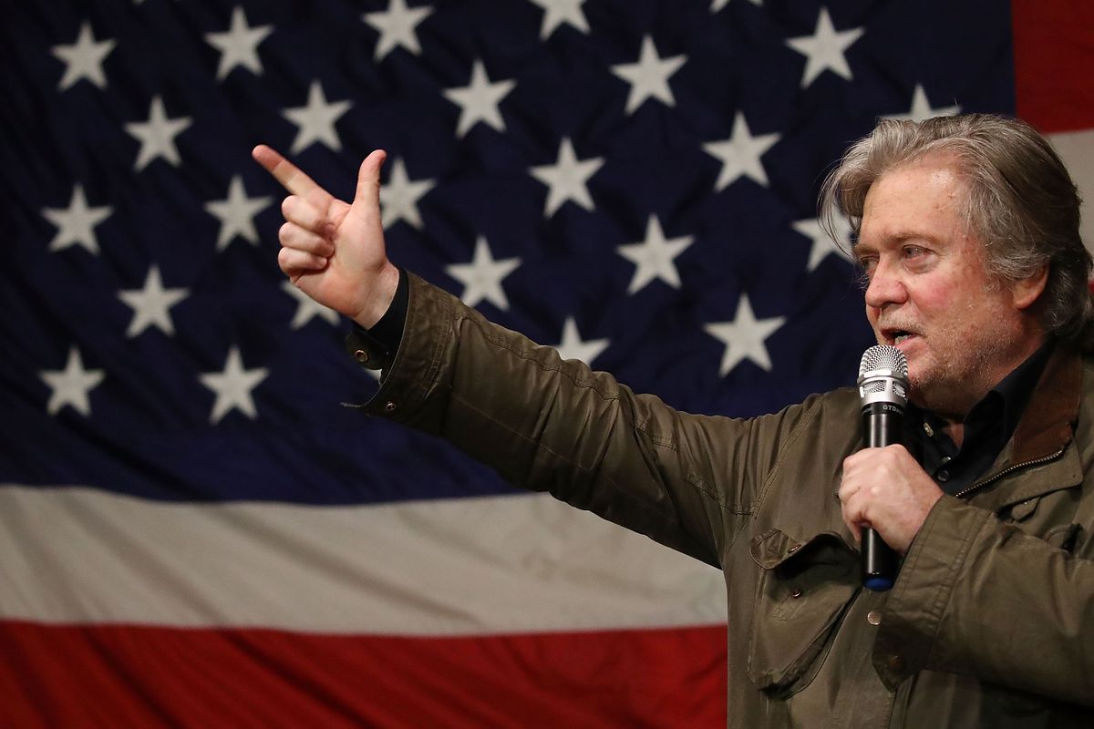 Steve Bannon stands on a stage in front of an American flag banner
