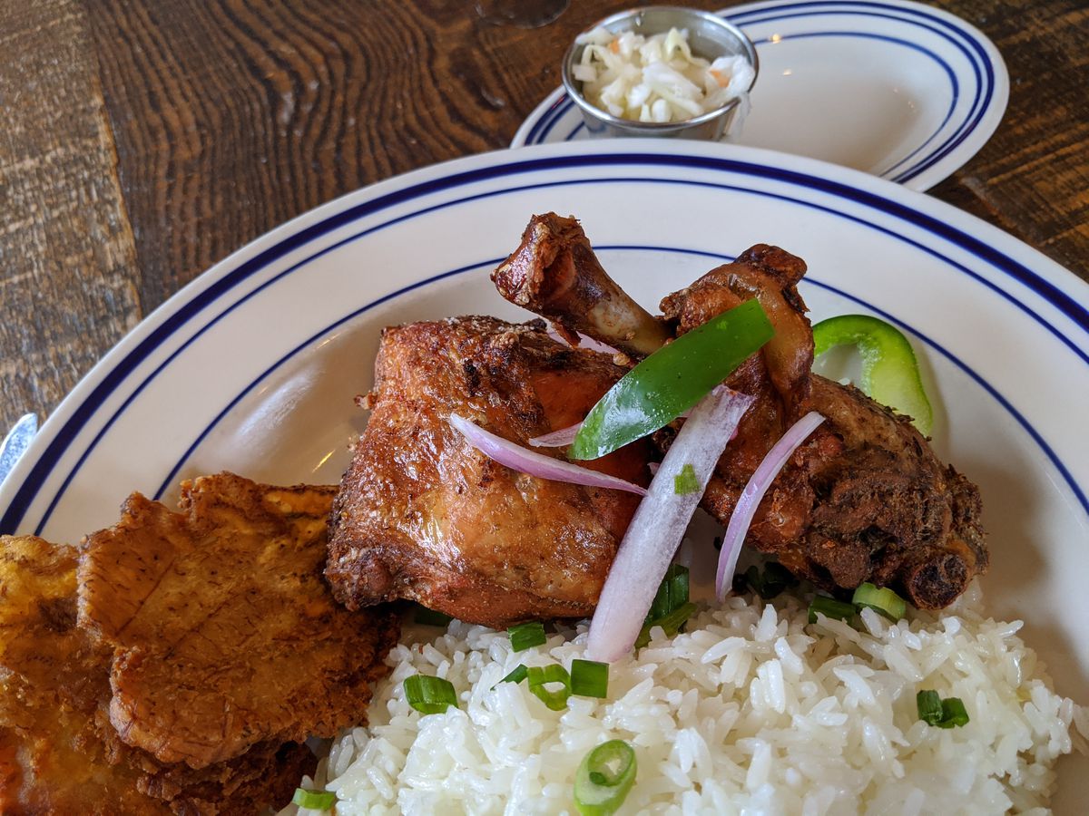 Two pieces of fried chicken with green plantains, rice, and slaw.