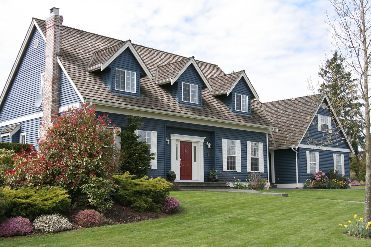 A navy blue home with large green yard and red front door. 