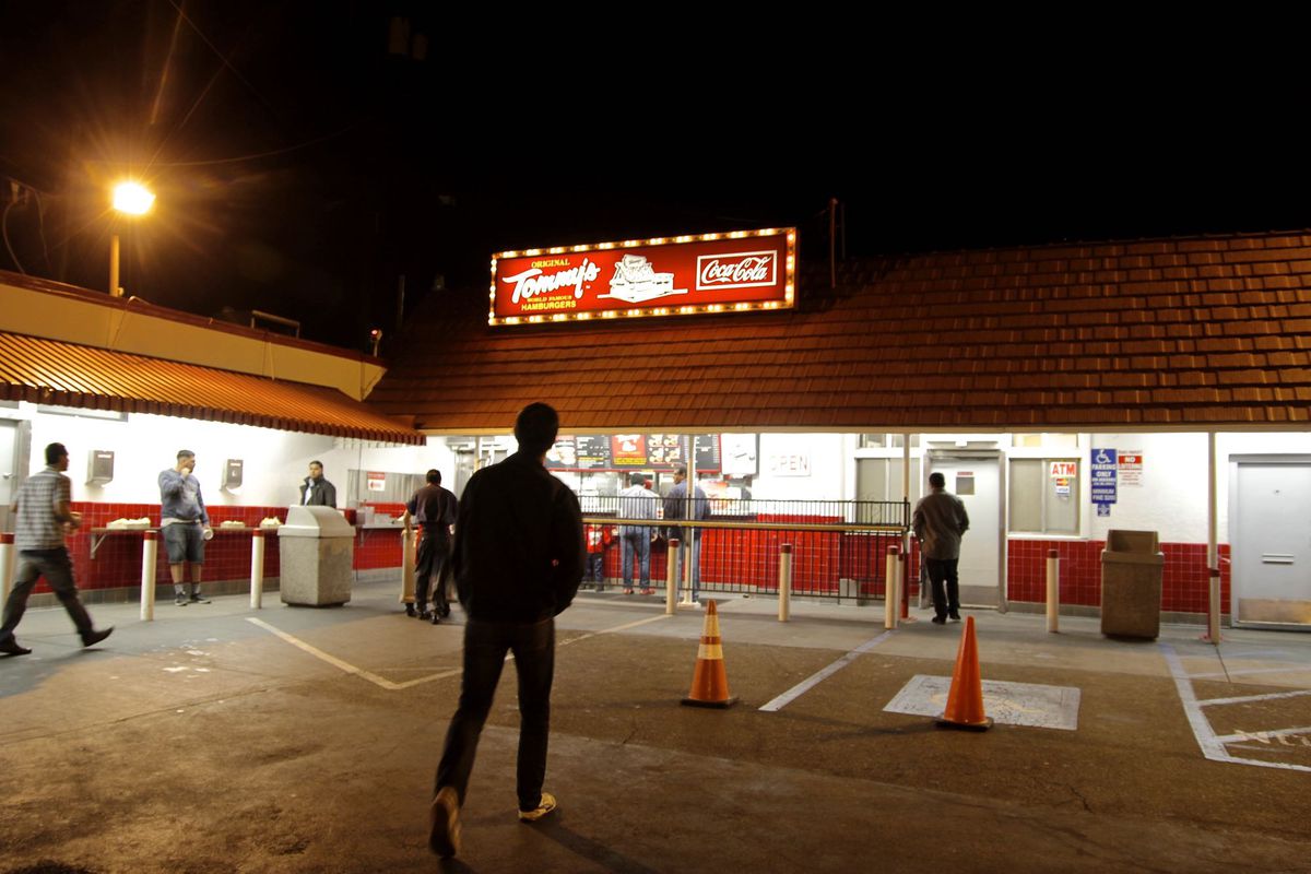 A shadowy figure stands at the historic burger stand Tommy’s late at night, surrounded by lights.