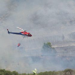 A helicopter prepares to drop water to prevent the fire from moving downhill toward homes.