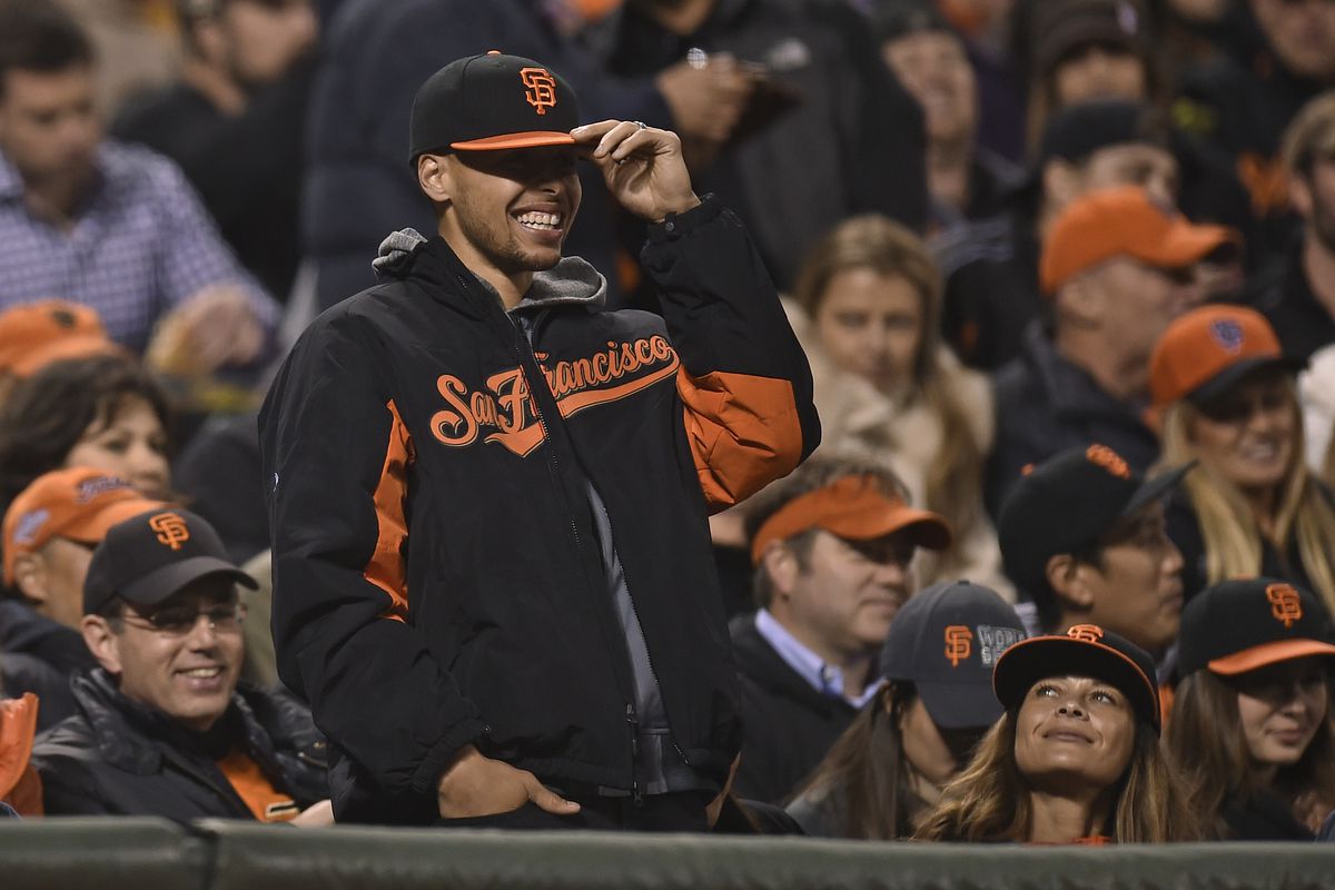 Steph Curry at a San Francisco Giants game, wearing Giants gear, holding his hat