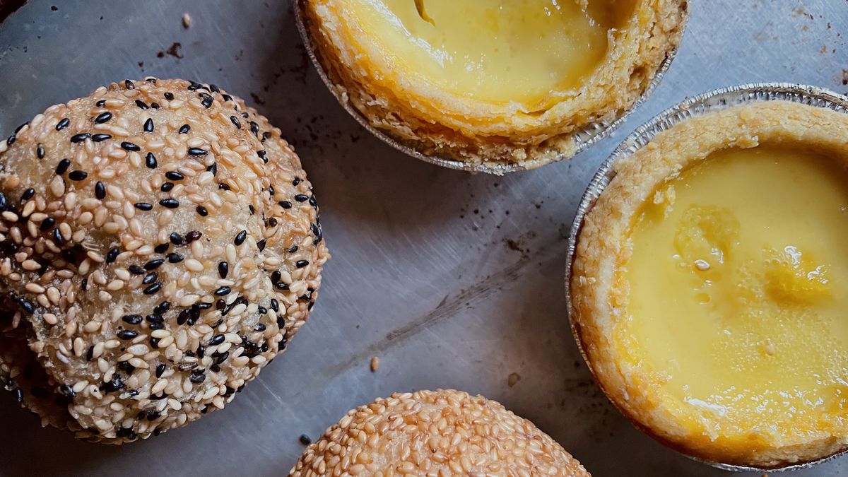 Two sesame balls and two bright yellow egg tarts against a grey background. 