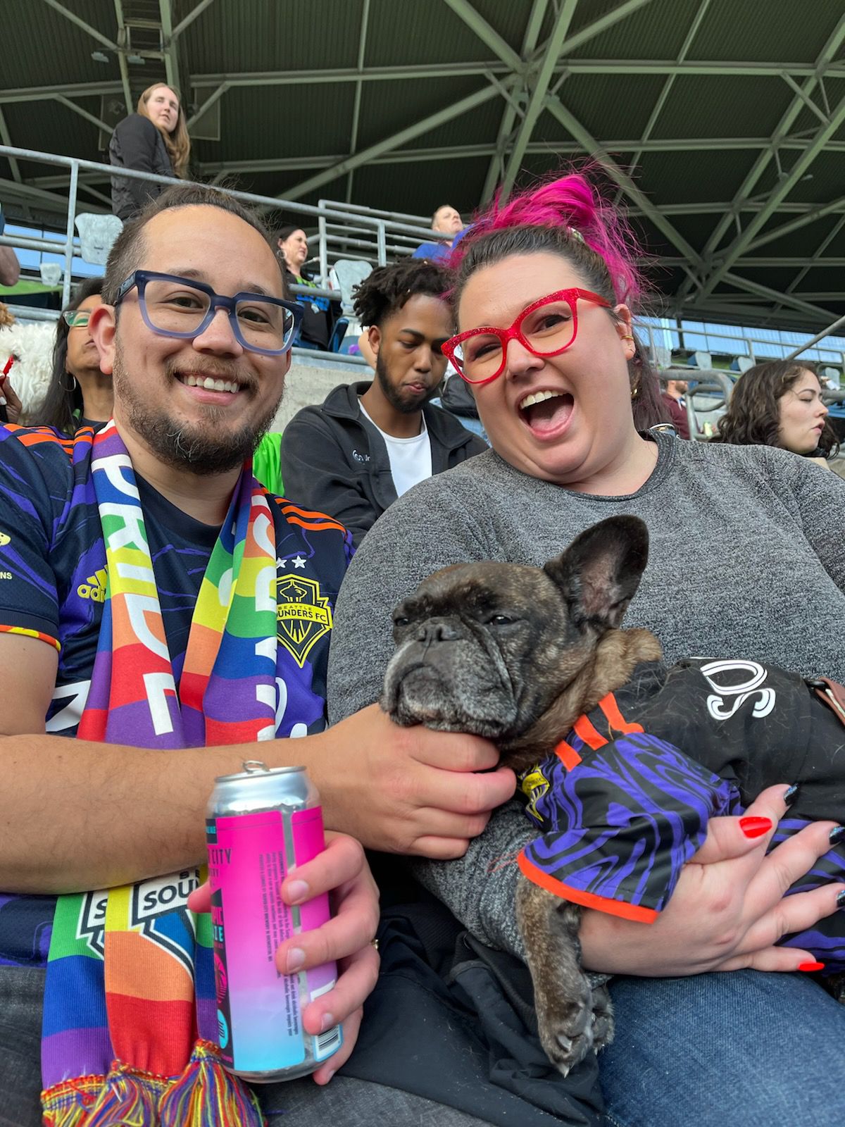 Kaitlin and Andrew Tingkang (the author and wife) with Sophie the french bulldog sitting in Kaitlin’s lap as Andrew scratches her chin. Andrew and Sophie are wearing matching Jimi Hendrix Sounders kits. Sophie’s were hand-made by her owner!