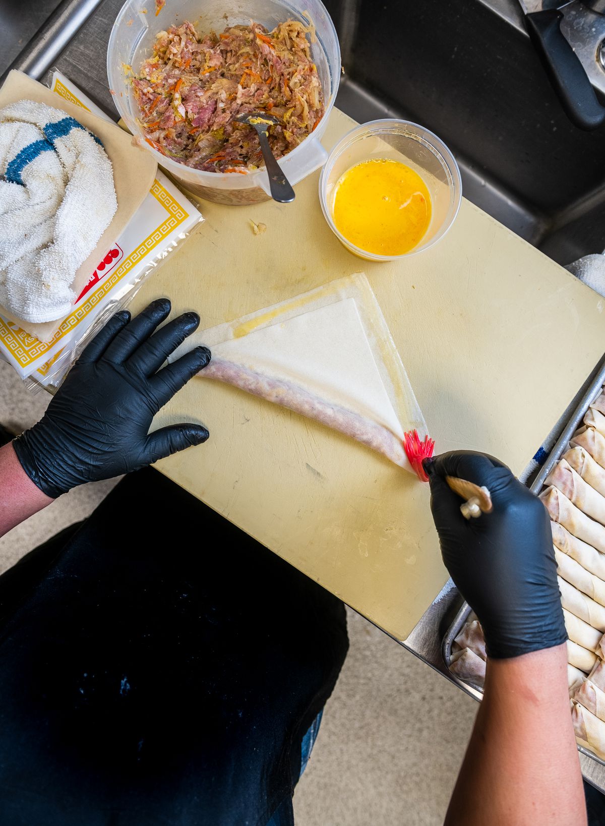 Javier Fernandez’s gloved hands roll a square wonton wrapper full of pork and shrimp to make lumpia, or Filipino egg rolls