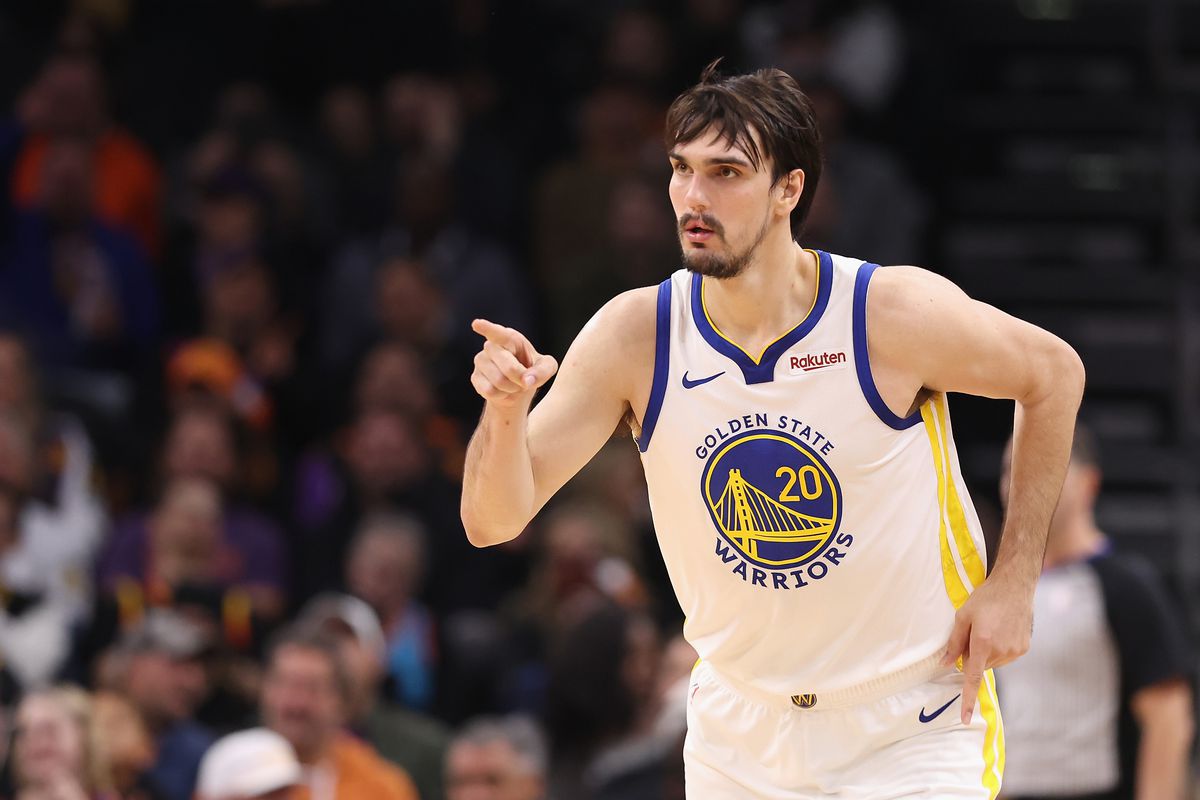 Dario Saric #20 of the Golden State Warriors reacts to a three-point shot against the Phoenix Suns during the first half of the NBA game at Footprint Center on December 12, 2023 in Phoenix, Arizona. The Warriors are wearing their white uniforms.