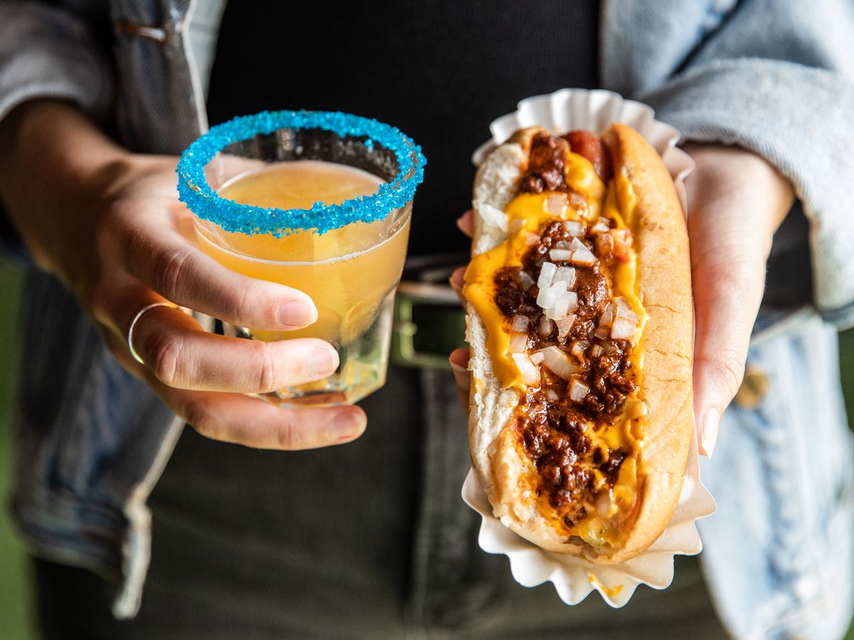 A cocktail rimmed with blue salt and a chili dog.