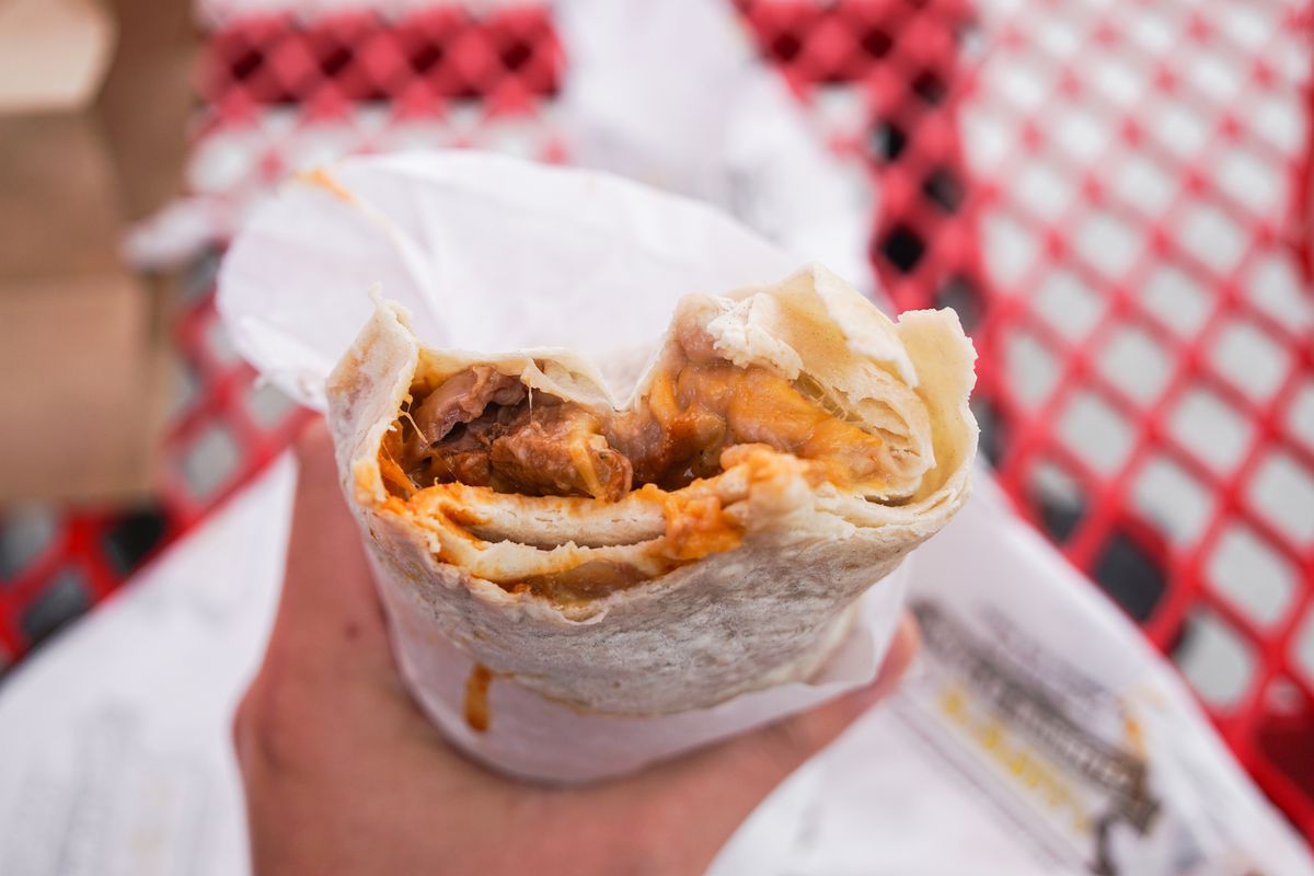 Half-bitten burrito wrapped in paper held by a hand.