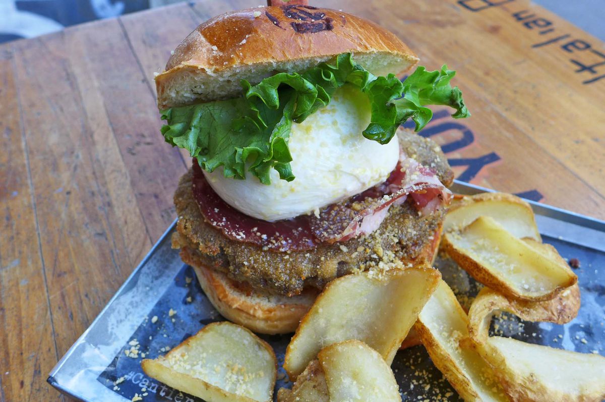 A piled high hamburger with a ball of burrata on top of the burger patty.