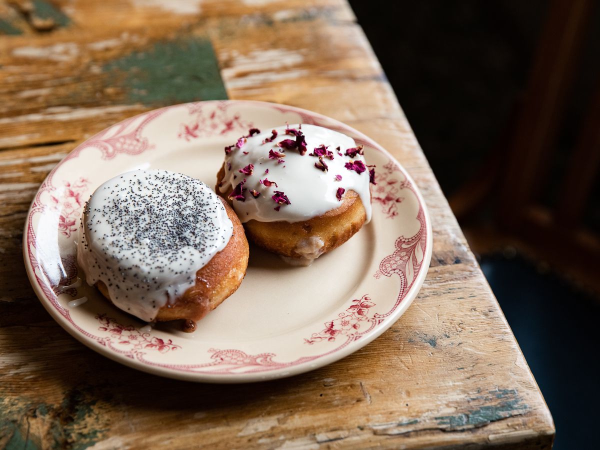 Two paczki on a plate covered in white icing with poppy seeds and rose petals sprinkled on top.