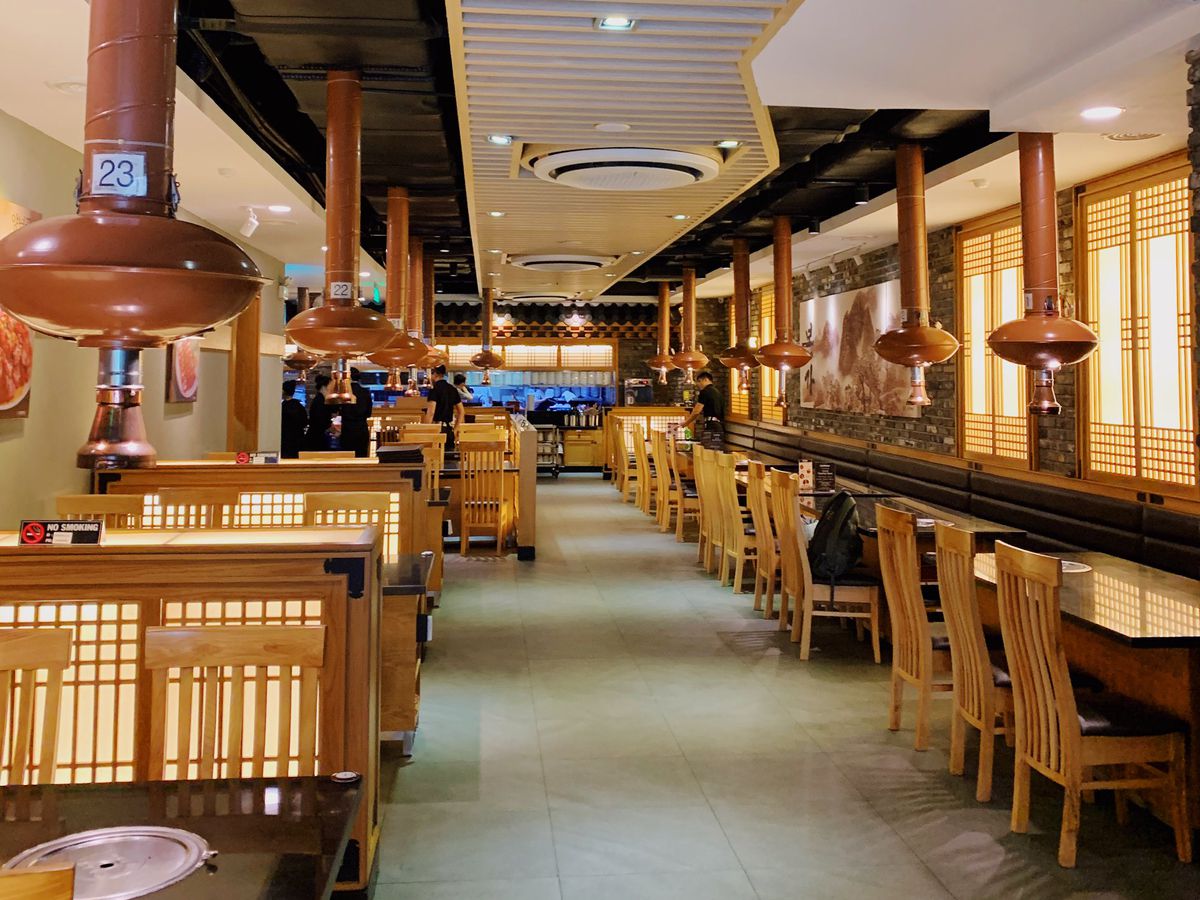 A restaurant interior with one long counter and tables outfitted with overhead vents.